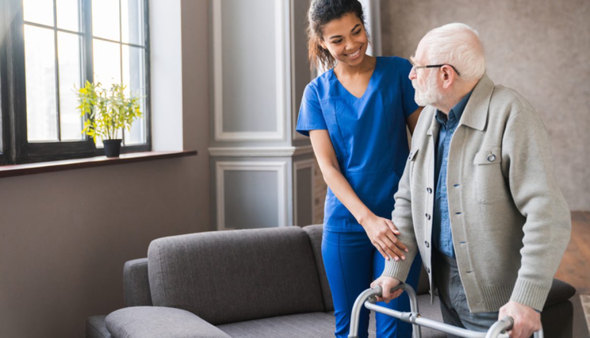 Portrait of an african young nurse helping old elderly disable man grandfather to walk using walker equipment in the bedroom. Senior patient of nursing home moving with walking frame and nurse support