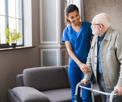 Portrait of an african young nurse helping old elderly disable man grandfather to walk using walker equipment in the bedroom. Senior patient of nursing home moving with walking frame and nurse support